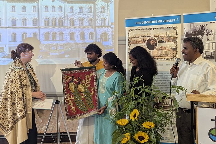 Gemeinsam mit den LMW-Freiwilligen aus Indien überreichte Rev. Dr. Thomas Kennedy ein textiles Wandbild, auf dem zwei Pfaue zu sehen sind. Einer symbolisiert die TELC und der andere das LMW.